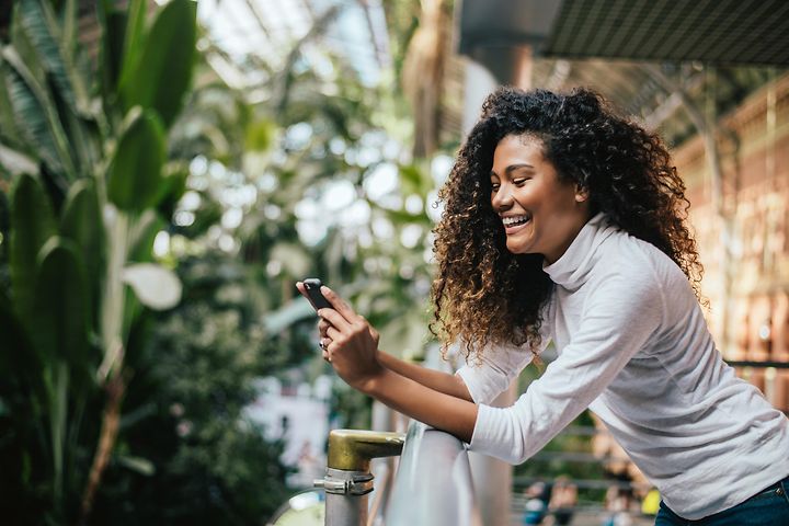 Smilende kvinne på balkong som ser på smarttelefon