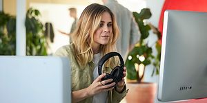 Woman working with PC using Microsoft 365 Office and holding headset in her hands